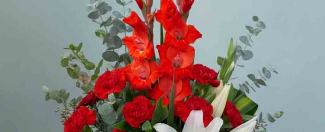 This elegant arrangement is filled with beautiful fresh flowers such as red gladioli and carnations with white asiatic lilies set amidst myrtle, sword fern, and salal in a decorative container.
